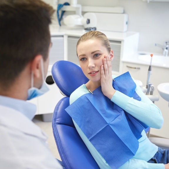 Young woman holding her cheek in pain while talking to dentist