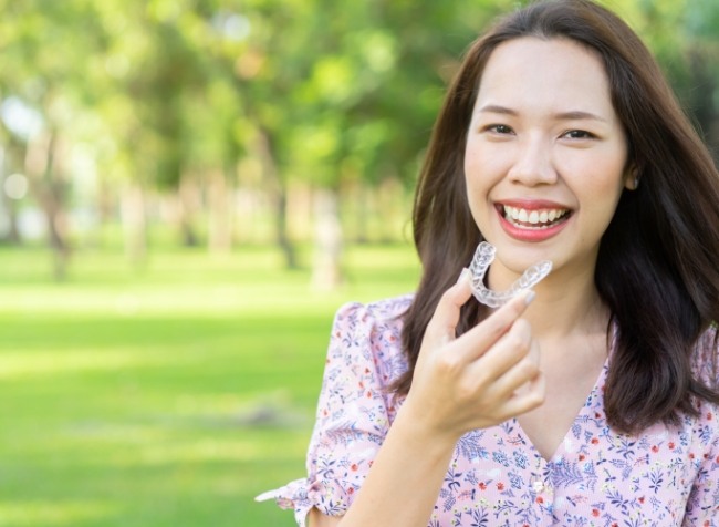 Smiling woman putting a clear aligner in her mouth outdoors