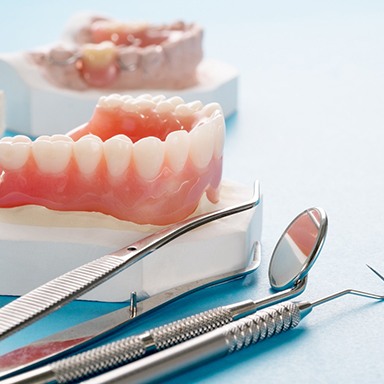 A close up of a full denture next to dental tools