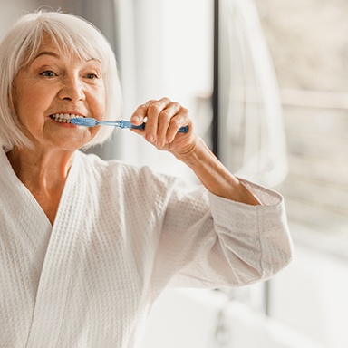 Woman smiling while brushing her teeth in bathroom