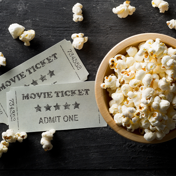 Two movie tickets on table next to bowl of popcorn